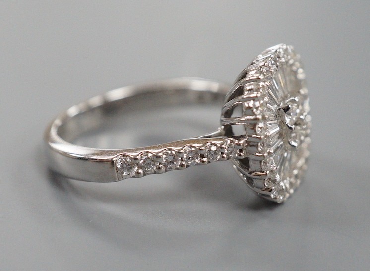 A modern 750 white metal, trapeze and round cut diamond set cushion shaped cluster dress ring, with diamond set shoulders, size M, gross weight 5.7 grams